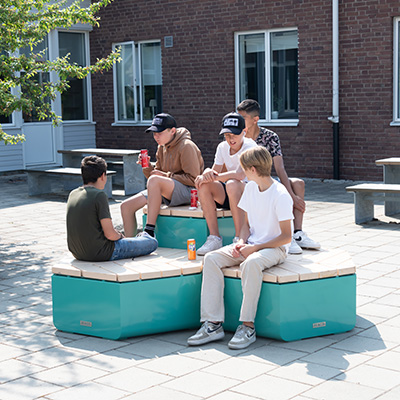 Un grupo de chicos jóvenes se relajan y socializan en una combinación de muebles rosenlund de exterior en color azul. Se trata de una disposición hexagonal de asientos informales.